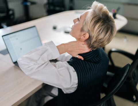 woman holds her neck while sitting at the office desk