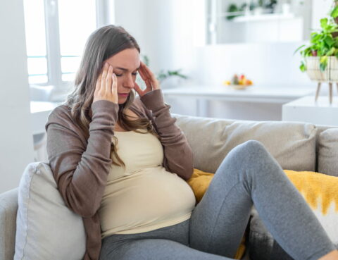 A pregnant woman is holding her hands on her head